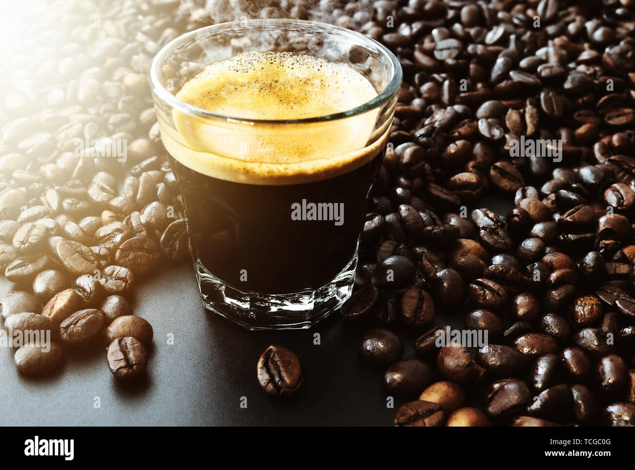 Glas mit dunklen heißen Espresso und gerösteten Kaffeebohnen auf Tisch gefüllt Stockfoto