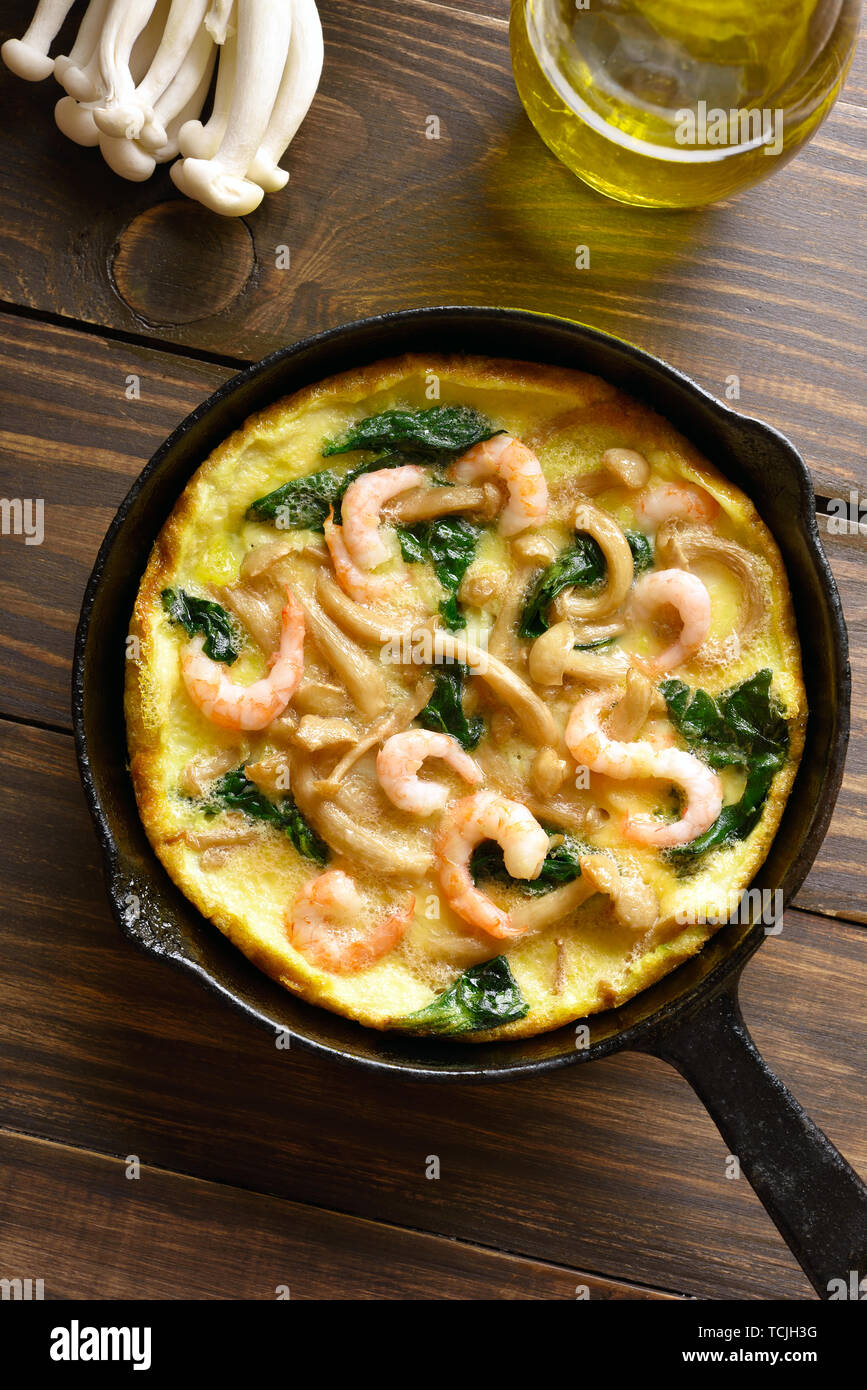 Pilze und Spinat frittata mit Garnelen in einer Pfanne auf Holz- Hintergrund. Ansicht von oben, flach Stockfoto