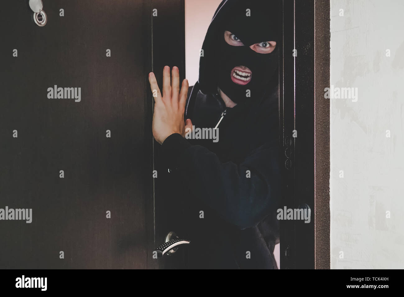 Eine böse Gangster in eine schwarze Maske bedeckte sein Gesicht brachen die Tür und brach in den Raum und die Bewohner bedroht. Konzept von Kriminalität und Gewalt. Stockfoto