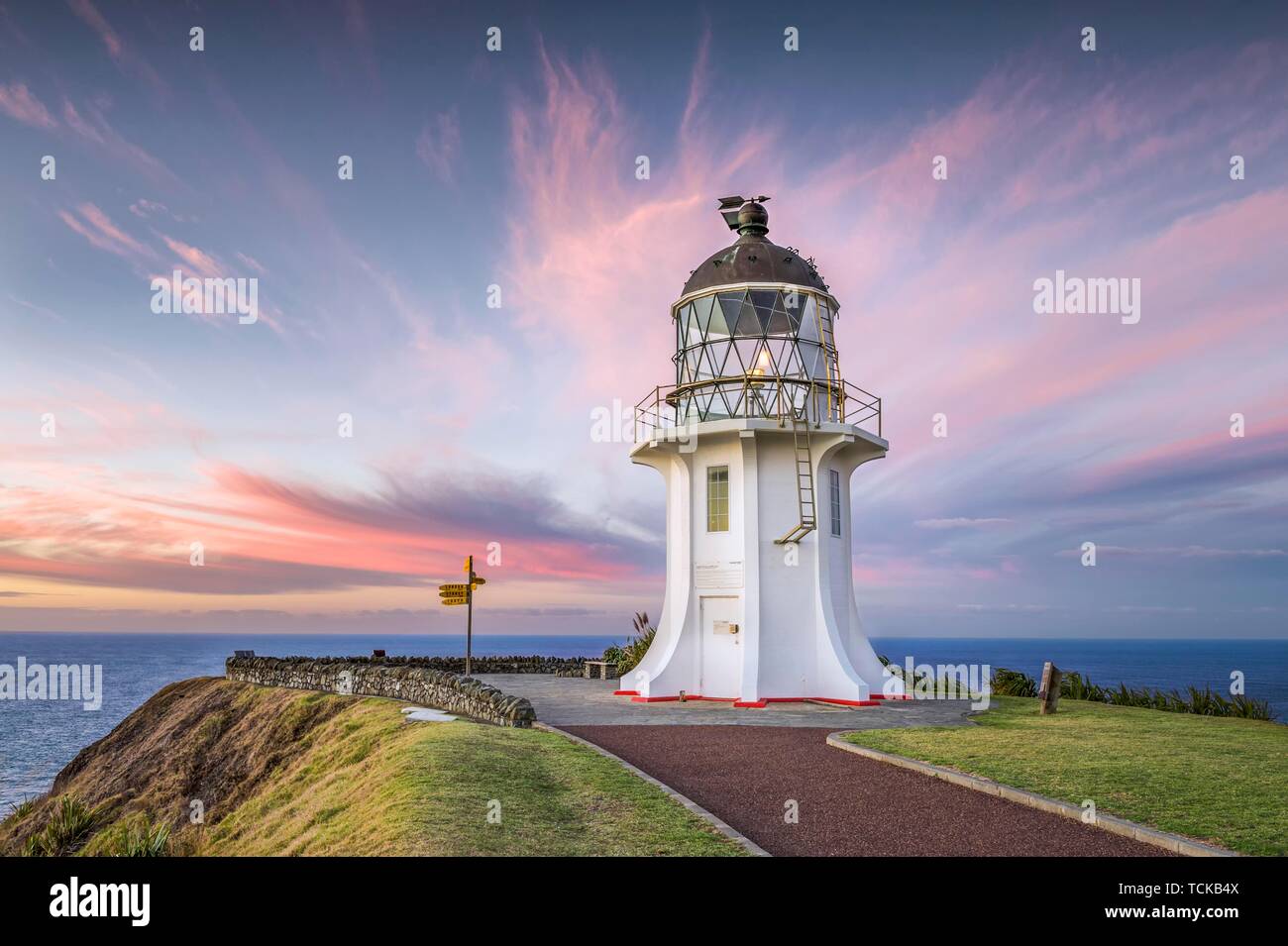 Leuchtturm mit Wegweiser am Cape Reinga bei Sonnenuntergang mit rosa Wolken, weit North District, Northland, North Island, Neuseeland Stockfoto