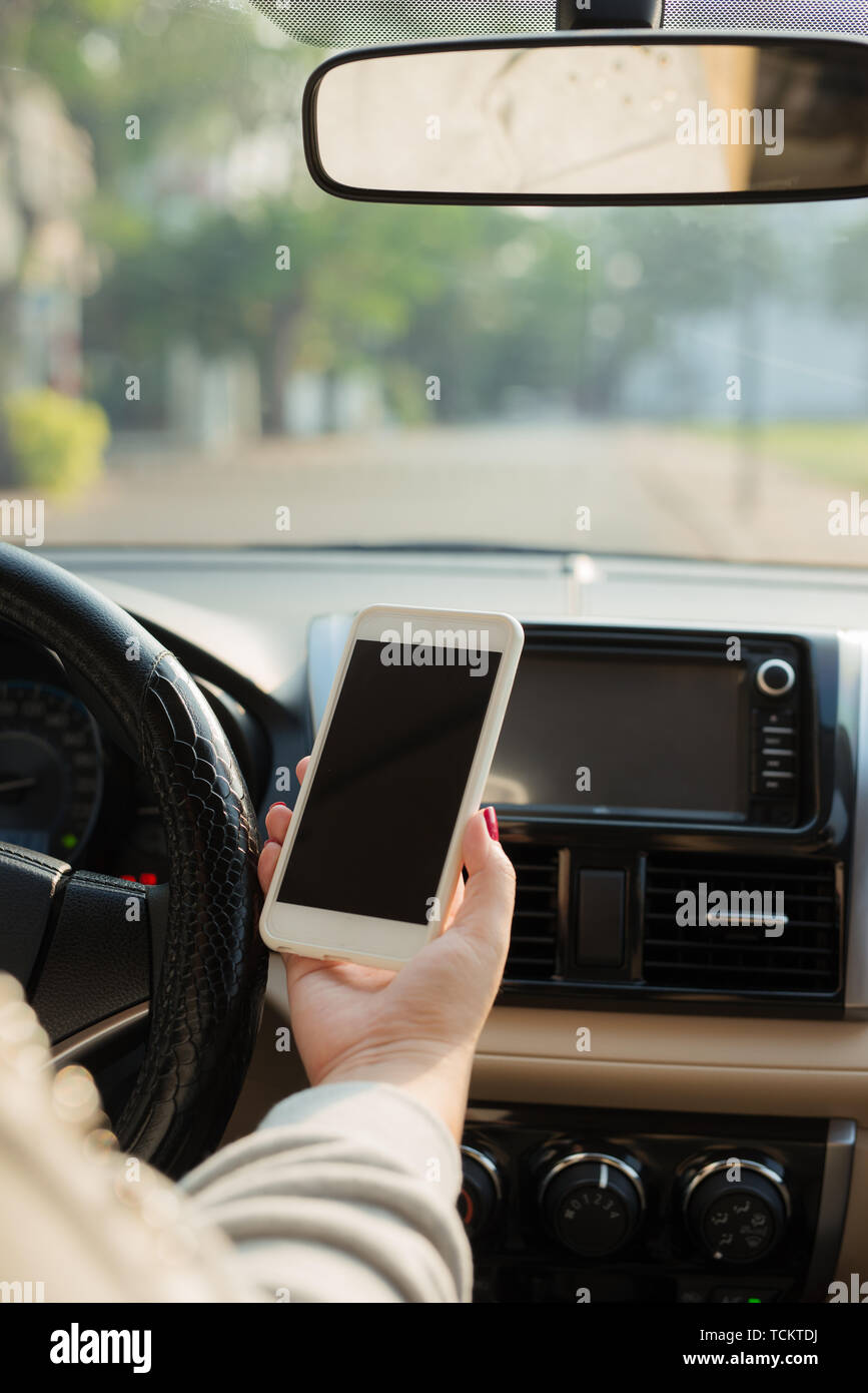 Junge Fahrerin mit Touch-Screen-Smartphone und Hand halten Lenkrad im Auto. Stockfoto