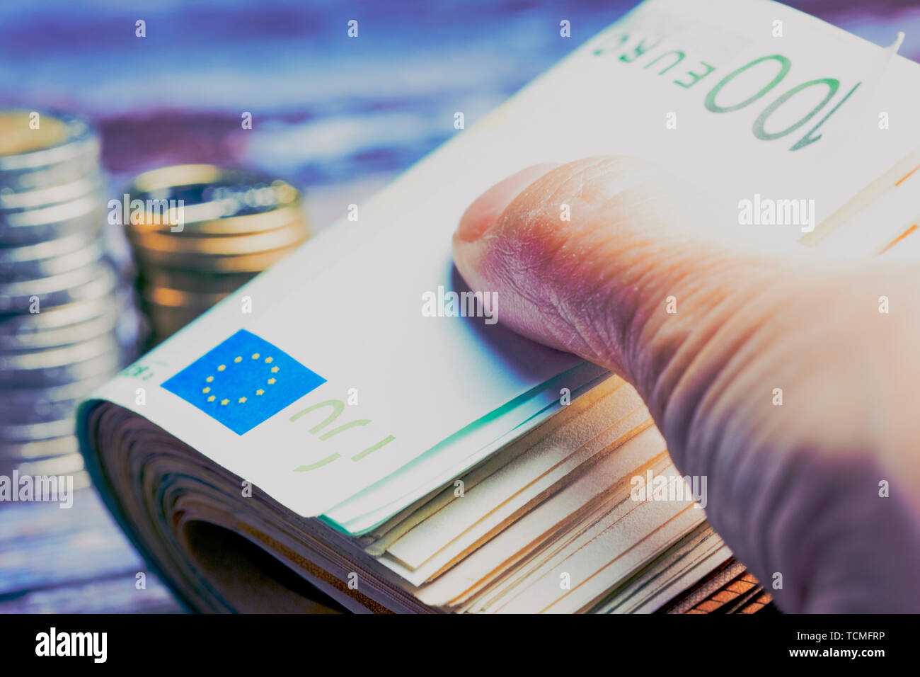 Weibliche Hand, und halten Sie mit Bündel von Euro-banknoten mit hundert Hinweis, im Hintergrund liegende verschwommen Euro-münzen, kalte farbe Stil Stockfoto