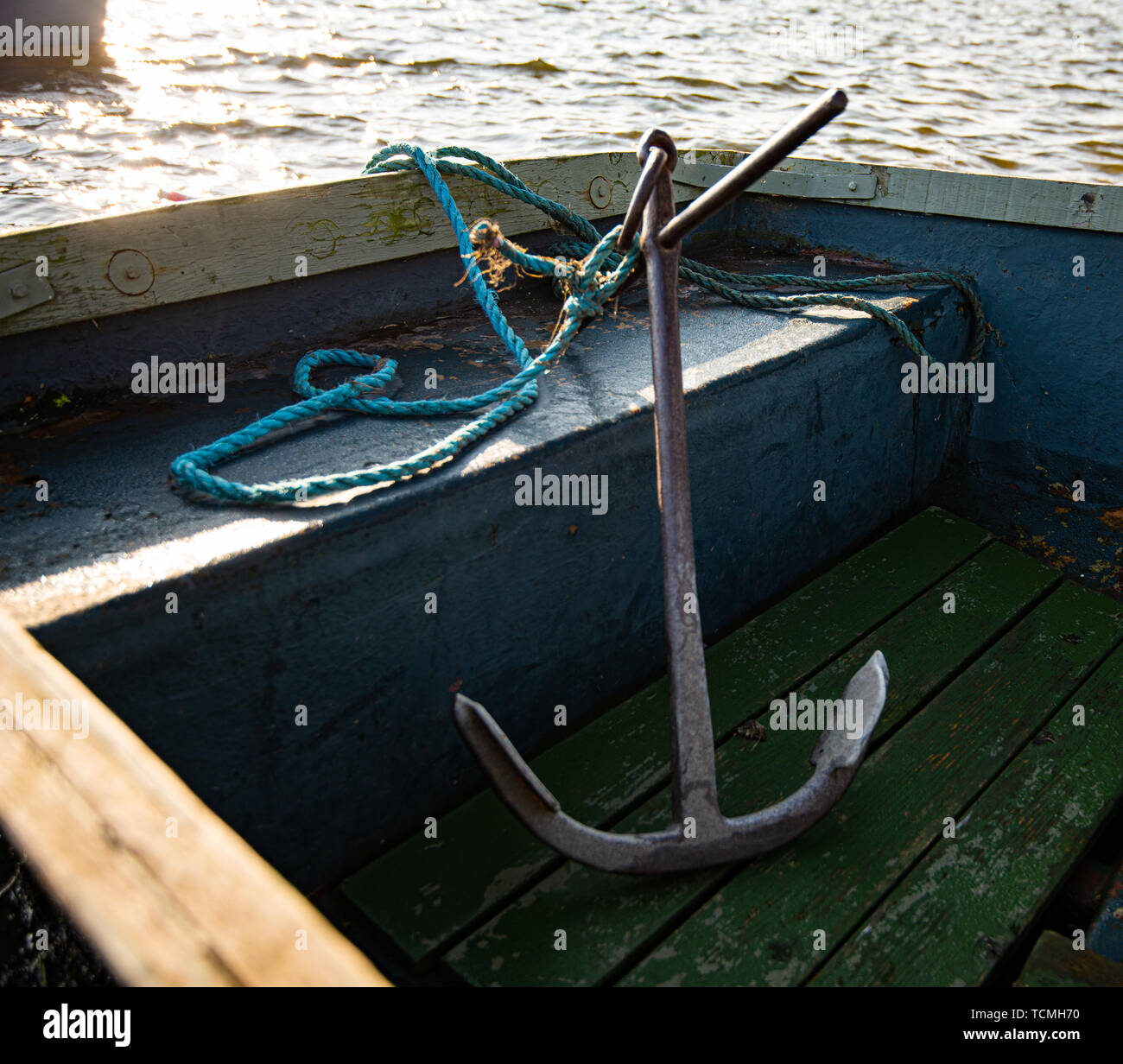 Ein großes metallisches Anker sitzt in einem kleinen blauen Ruderboot. Während einer frühen Sonnenuntergang auf einem kleinen See genommen Stockfoto