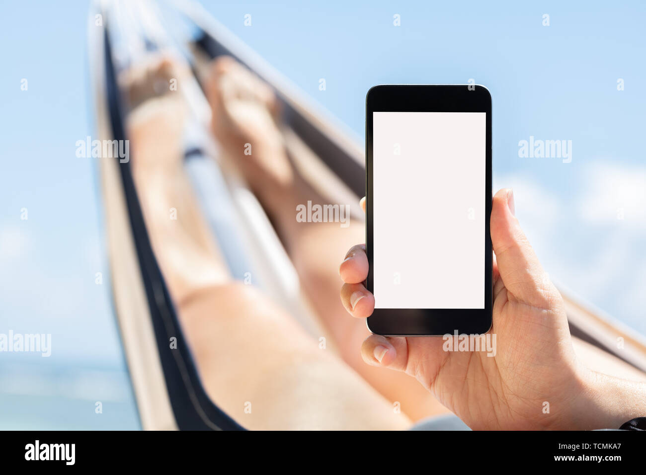 Junge Frau liegend auf Hängematte mit Handy mit weißen Bildschirm gegen den blauen Himmel Stockfoto