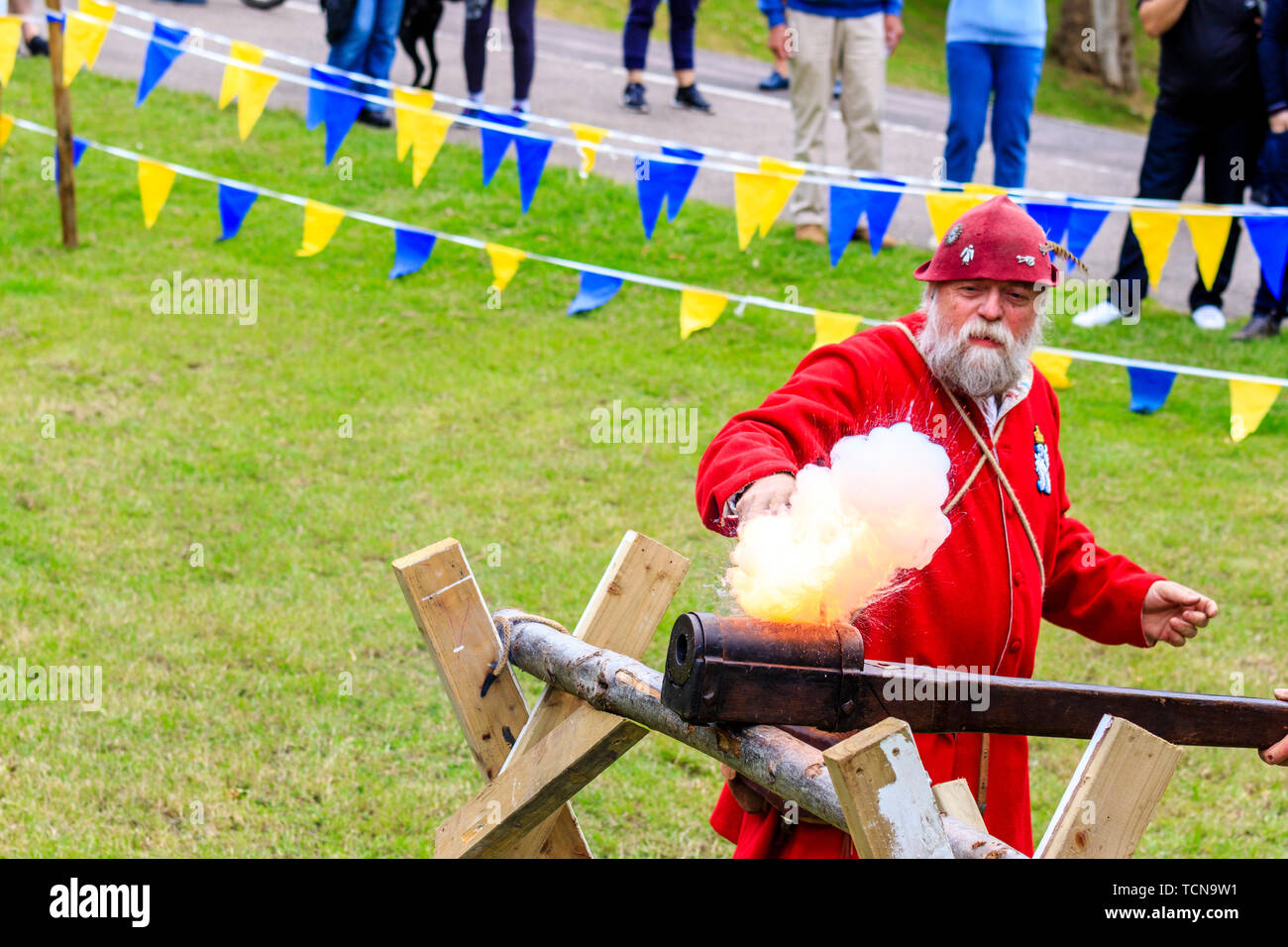Le mittelalterliche Wochenende Re-enactment Veranstaltung am Sandwich Stadt in England. Mann gekleidet in mittelalterlichen Roten gunner Outfit und feuerte eine hand Cannon an einer Halterung montiert. Rauch und Feuer. Stockfoto