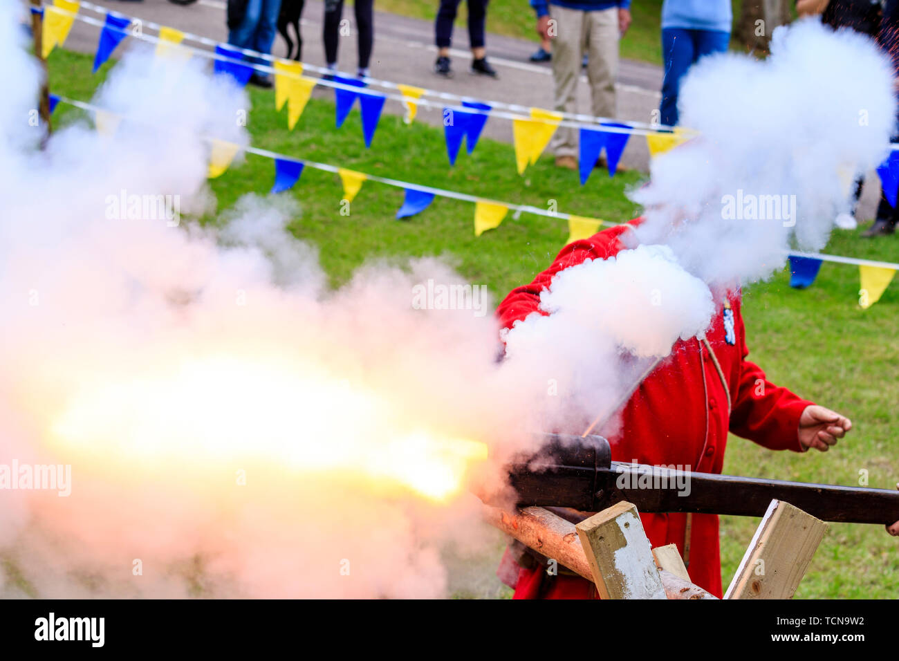 Le mittelalterliche Wochenende Re-enactment Veranstaltung am Sandwich Stadt in England. Mann gekleidet in mittelalterlichen Roten gunner Outfit und feuerte eine hand Cannon an einer Halterung montiert. Rauch und Feuer. Stockfoto