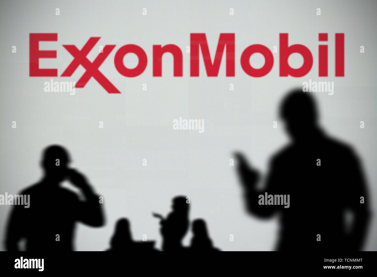 Die ExxonMobil Logo ist auf einen LED-Bildschirm im Hintergrund, während eine Silhouette Person ein Smartphone verwendet im Vordergrund (nur redaktionelle Nutzung) Stockfoto