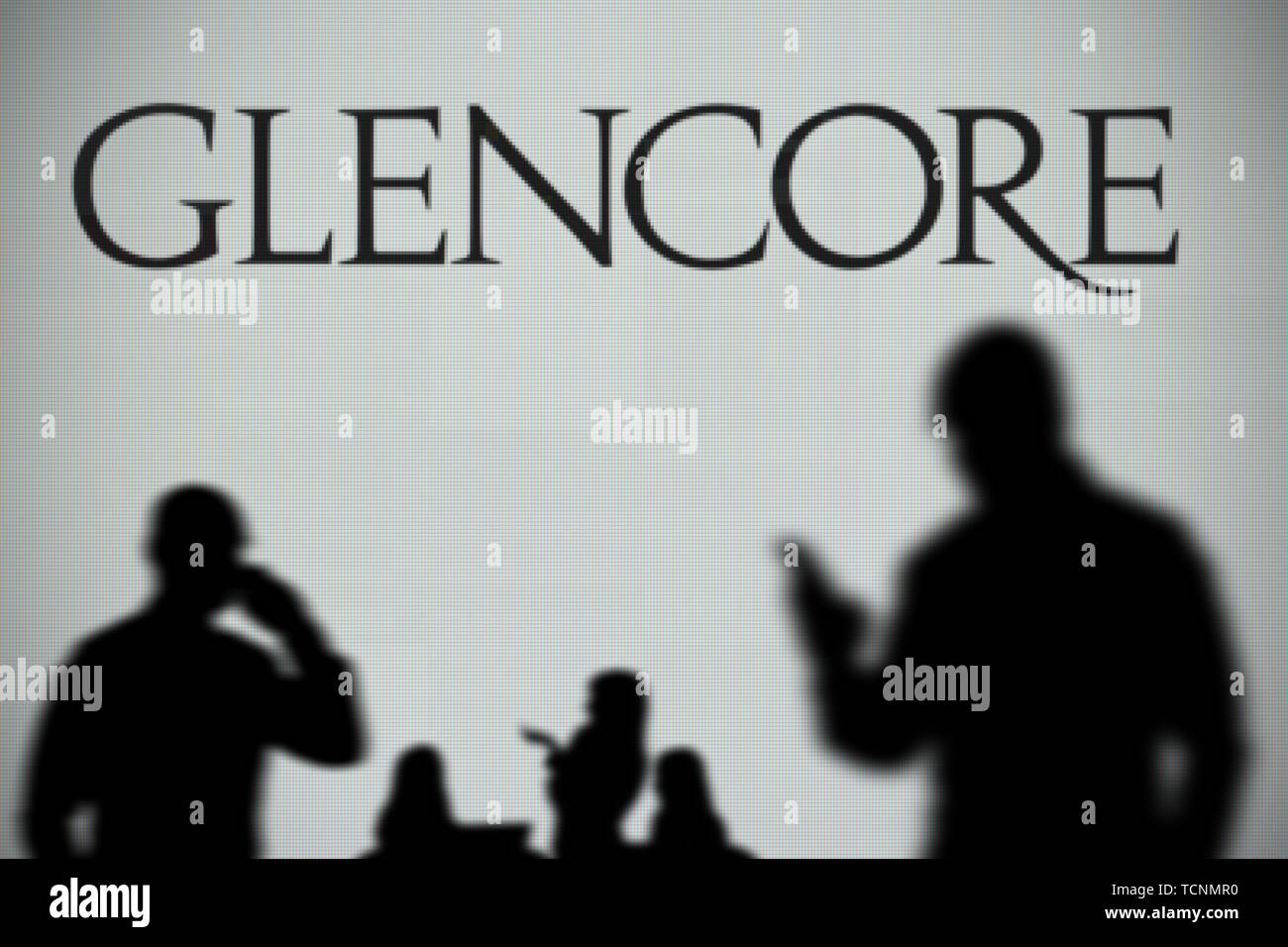 Die glencore Logo ist auf einen LED-Bildschirm im Hintergrund, während eine Silhouette Person ein Smartphone verwendet im Vordergrund (nur redaktionelle Nutzung) Stockfoto
