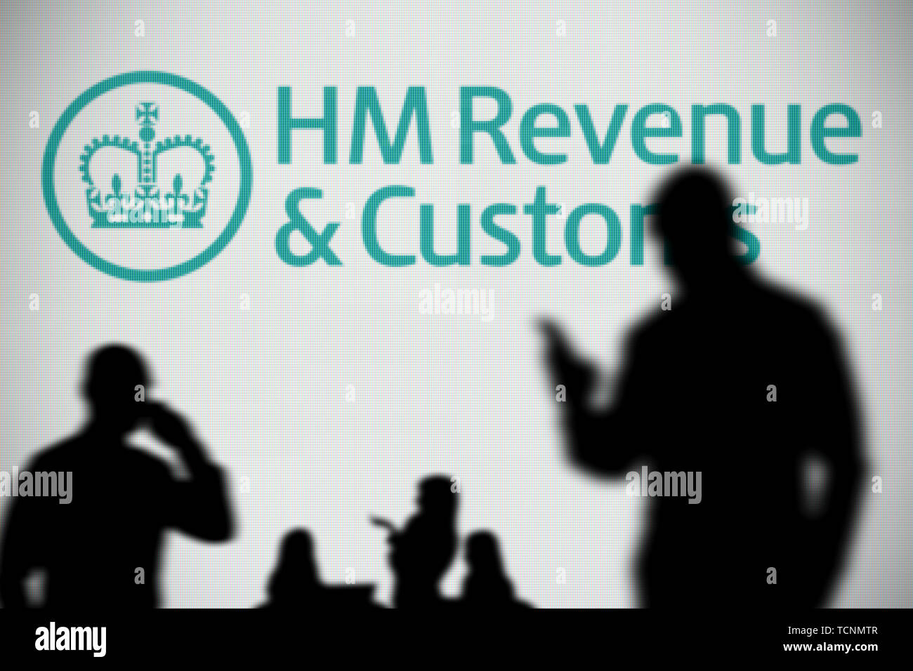 Die hmrc Logo ist auf einen LED-Bildschirm im Hintergrund, während eine Silhouette Person ein Smartphone verwendet im Vordergrund (nur redaktionelle Nutzung) Stockfoto