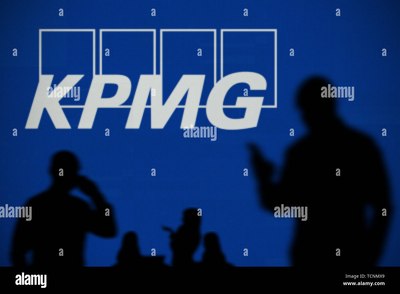 Die KPMG-Logo ist auf einen LED-Bildschirm im Hintergrund, während eine Silhouette Person ein Smartphone verwendet im Vordergrund (nur redaktionelle Nutzung) Stockfoto