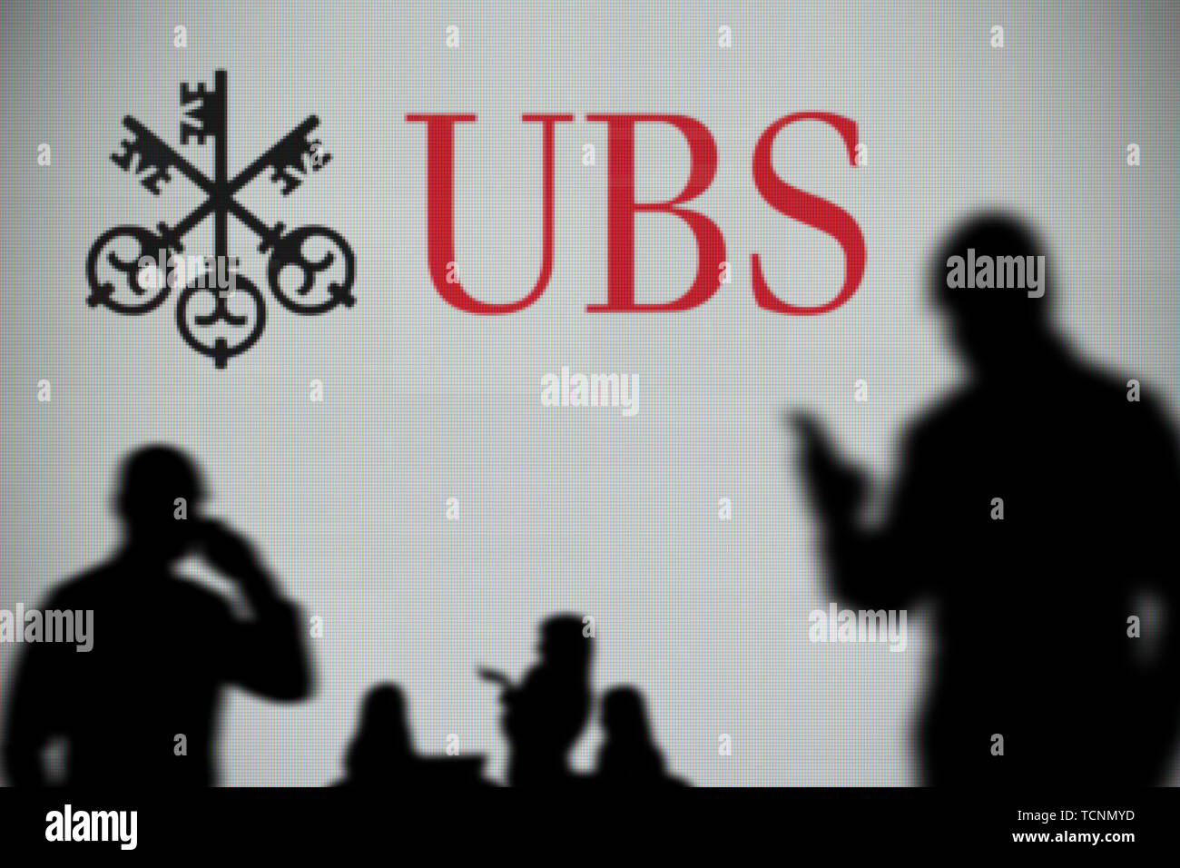 Die UBS-Logo ist auf einen LED-Bildschirm im Hintergrund, während eine Silhouette Person ein Smartphone verwendet im Vordergrund (nur redaktionelle Nutzung) Stockfoto
