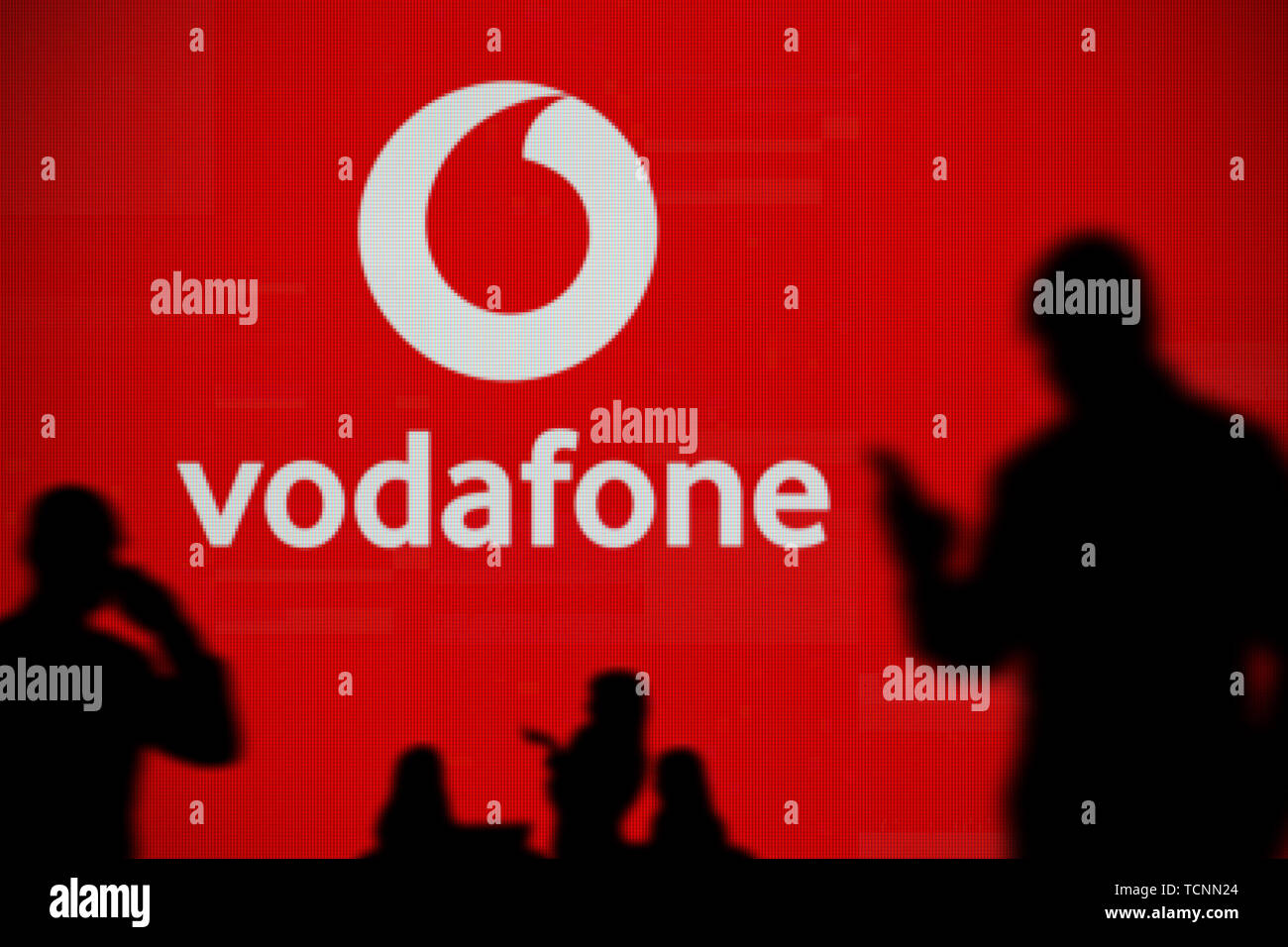 Die Vodafone Logo ist auf einen LED-Bildschirm im Hintergrund, während eine Silhouette Person ein Smartphone verwendet im Vordergrund (nur redaktionelle Nutzung) Stockfoto