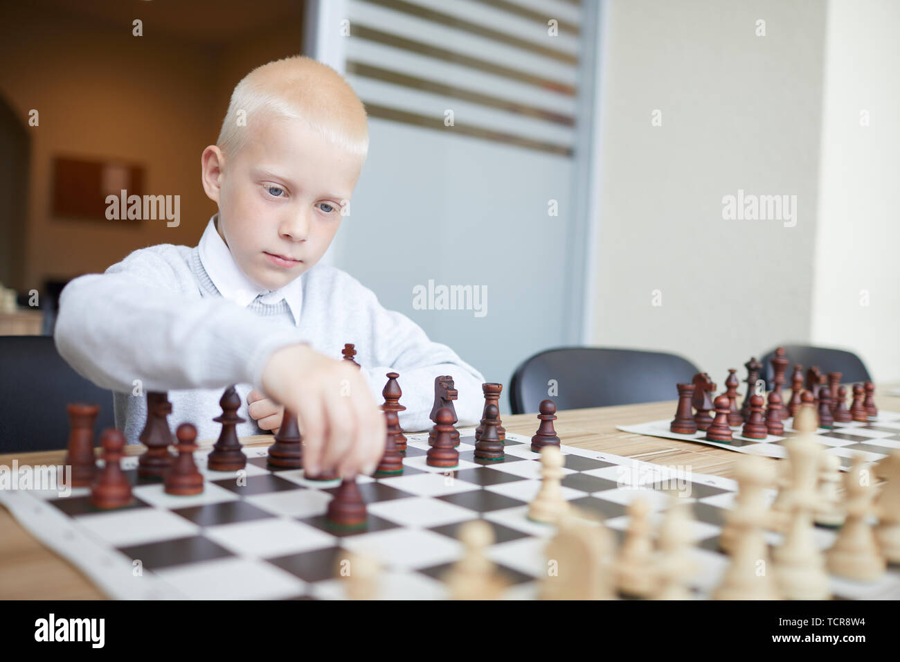Blonde Schüler in weißem Hemd, erste Schach bewegen im Spiel mit imaginären Gegner Stockfoto