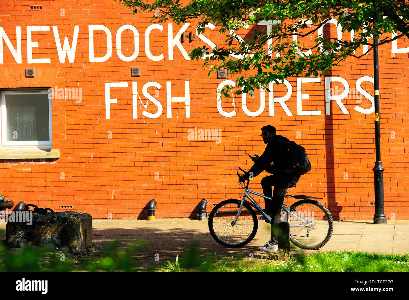 Ein Mann auf dem Fahrrad, der gegen die Wand von Fischcurers in Fleetwood, Großbritannien, gekleidet ist Stockfoto