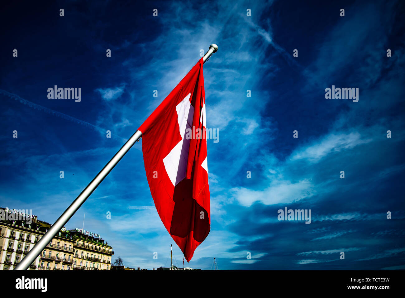Schweizer Fahne auf windigen Tag, Genfer See im Hintergrund, weiße rote Kreuz, blauer Himmel mit stürmischen Wolken Stockfoto