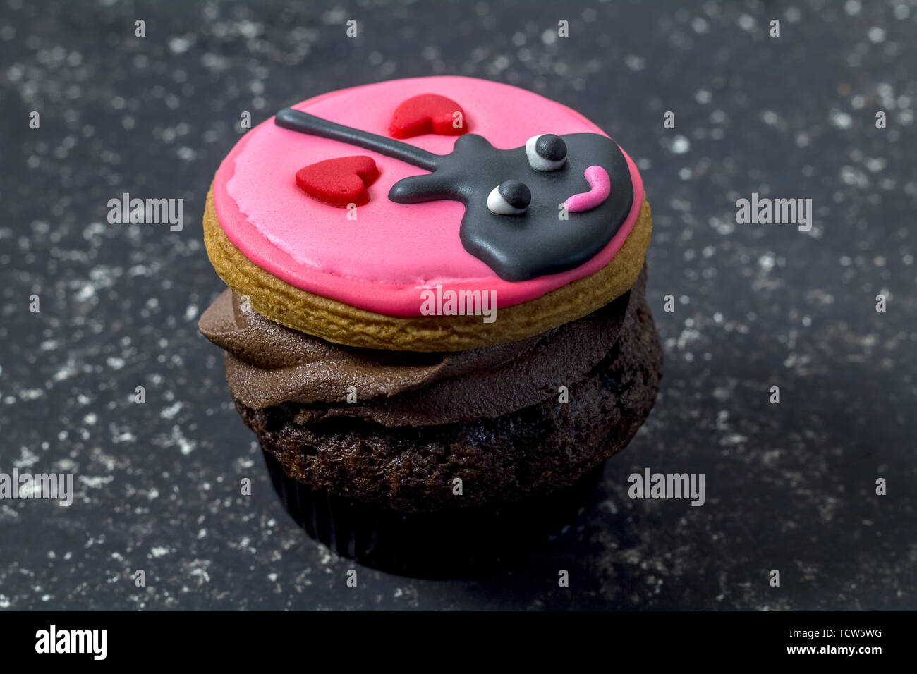Valentines Tag Cupcake auf Schwarz gesprenkelter Hintergrund isoliert - Spaß Cupcake mit schwarzen Gitarre und zwei Herzen mit rosa Zuckerglasur auf Schokolade dekoriert Stockfoto