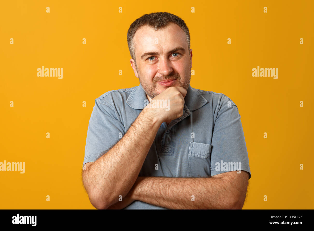 Nachdenklicher Mann mit der Hand am Kinn und Kamera. Gelber Hintergrund. Closeup Portrait. Stockfoto
