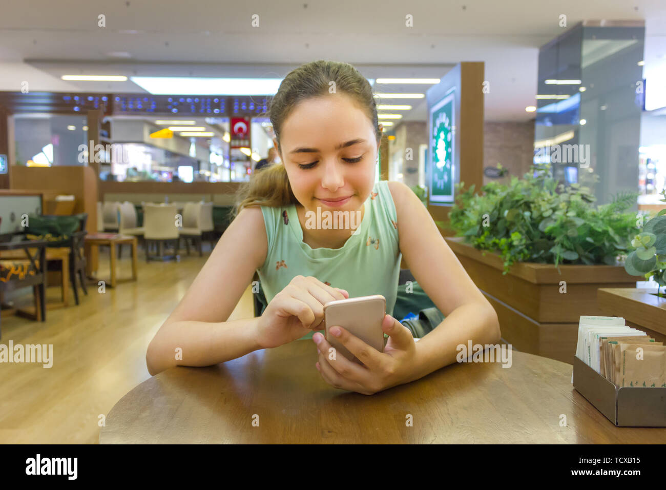 Junge schöne jugendlich Mädchen beobachten lustige Videos auf dem Smartphone im Cafe in der Mall Stockfoto