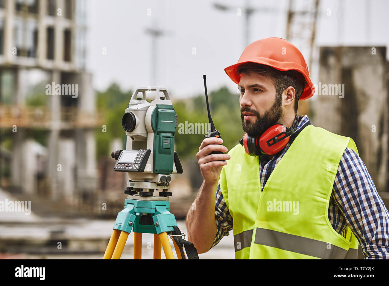 Genaue Messungen. Vermessungsingenieur in Schutzkleidung und Roten Helm mit geodätischen Anlagen und die Unterhaltung von Walkie talkie bei cons stehend Stockfoto