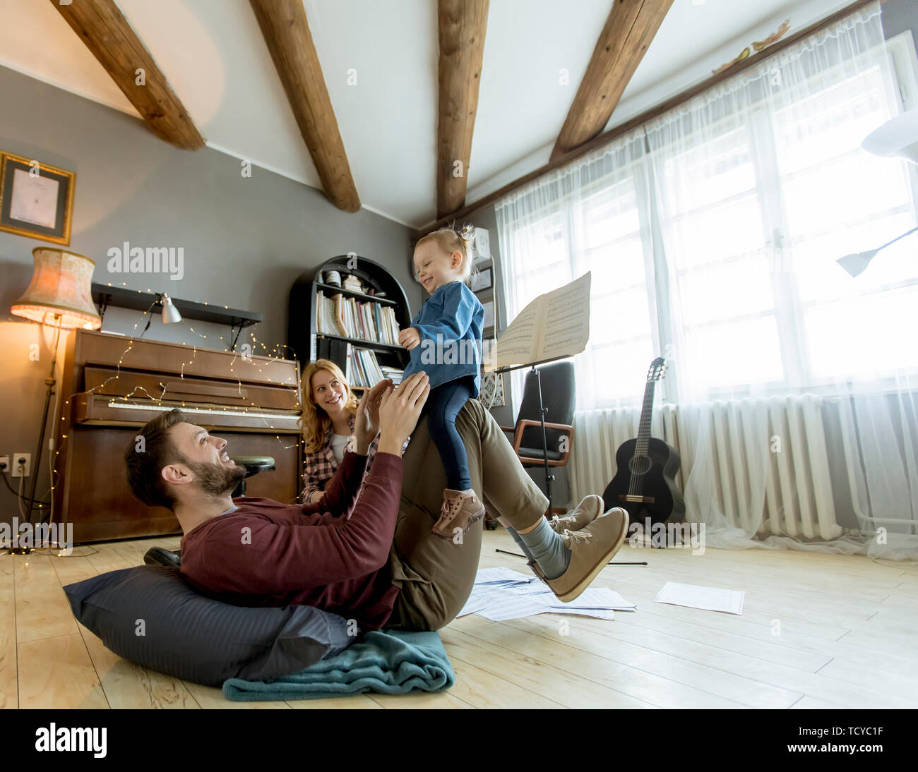 Glückliche junge Familie mit netten Mädchen spielen auf dem Boden im rustikalen Zimmer Stockfoto