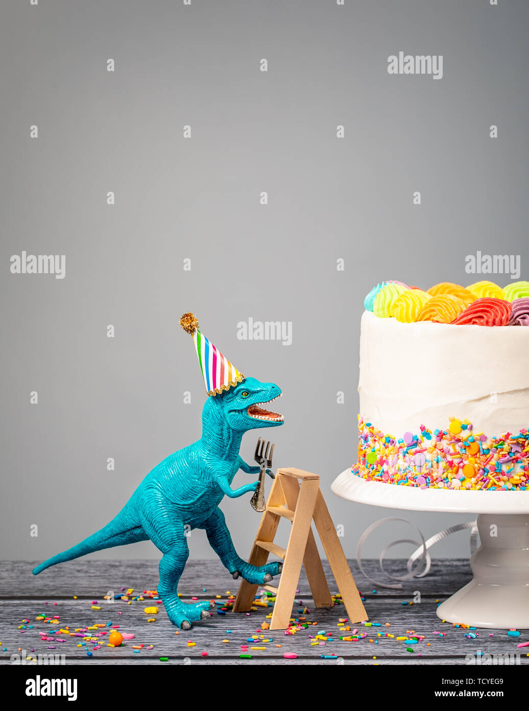 Dumme Spielzeug Dinosaurier einen Hut tragen und halten eine Gabel klettern eine Leiter einen Geburtstagskuchen auf grauem Hintergrund Stockfoto