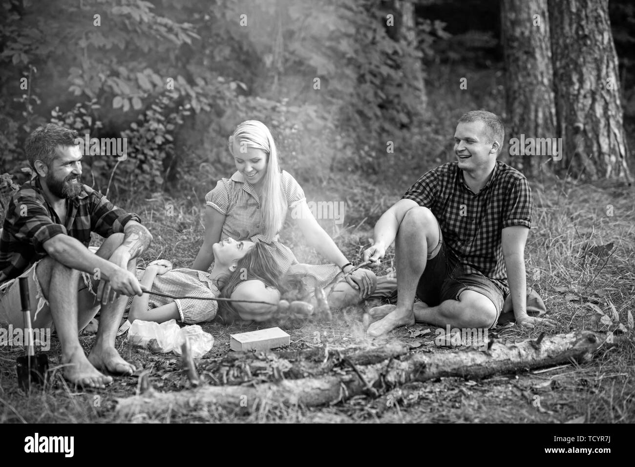 Grillen Würstchen über dem Lagerfeuer, Camper braten Würstchen auf toasten Sticks. Kamin mit Freunden oder Touristen sitzen in der Nähe der Flamme. Stockfoto