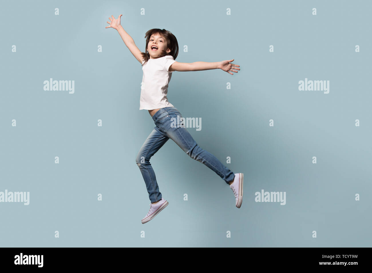 Volle Länge lustige kleine Mädchen auf blauem Hintergrund isoliert springen Stockfoto