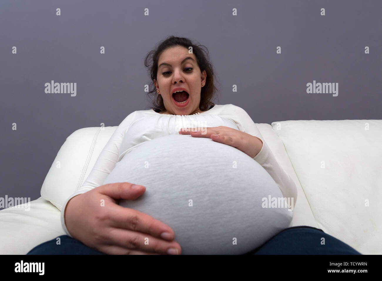 Humorvoll entsetzte Reaktion der schwangeren Mutter zu ihren großen wachsenden Bauch Stockfoto