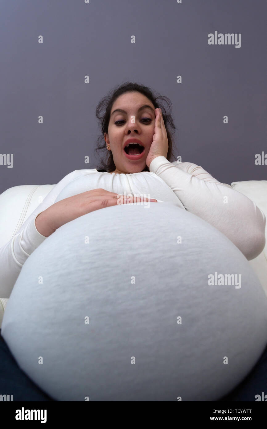 Humorvoll entsetzte Reaktion der schwangeren Mutter zu ihren großen wachsenden Bauch Stockfoto