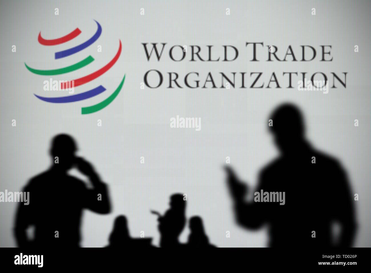 Die World Trade Organisation Logo ist auf einen LED-Bildschirm in der Silhouette gesehen, während eine Person ein Smartphone verwendet im Vordergrund (nur redaktionelle Nutzung) Stockfoto