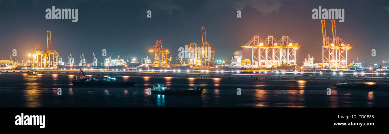 Panoramablick über Kräne laden Versand Container in der Frachtschifffahrt Hafen bei Nacht, Banner Größe. Import oder Export, Logistik Industrie Stockfoto