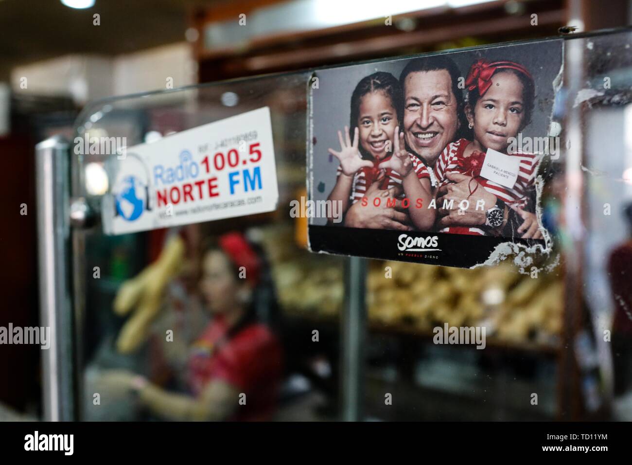 05. Juni 2019, Venezuela, Caracas: 'Wir sind Liebe', steht unter dem Bild des verstorbenen Präsidenten Hugo Chavez (M.) mit zwei Kindern in der Bäckerei 'La Minka, die von Anhängern der Regierung. Alle Mitarbeiter haben den Beruf in der Bäckerei gelernt. Der jüngste Teil der Mannschaft für 15 Tage. Die ehemalige private Bäckerei war 'Mansion Bäckerei' genannt. Jetzt rund 6.000 Stücke Brot gibt es jeden Tag bei der Preise durch den Staat produziert. Das Land mit den größten Ölreserven der Welt befindet sich in einem dramatischen Niedergang. Geld Abwertung ist die höchste in der Welt, für viele Menschen essen ist unaffo Stockfoto
