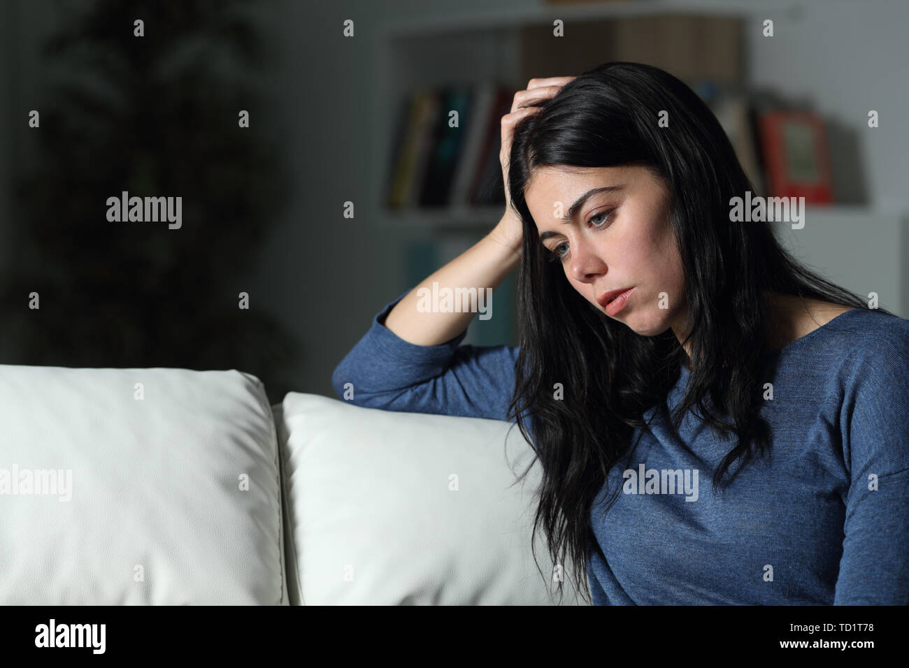 Traurige Frau denken weg schauen sitzen auf einer Couch in der Nacht zu Hause Stockfoto