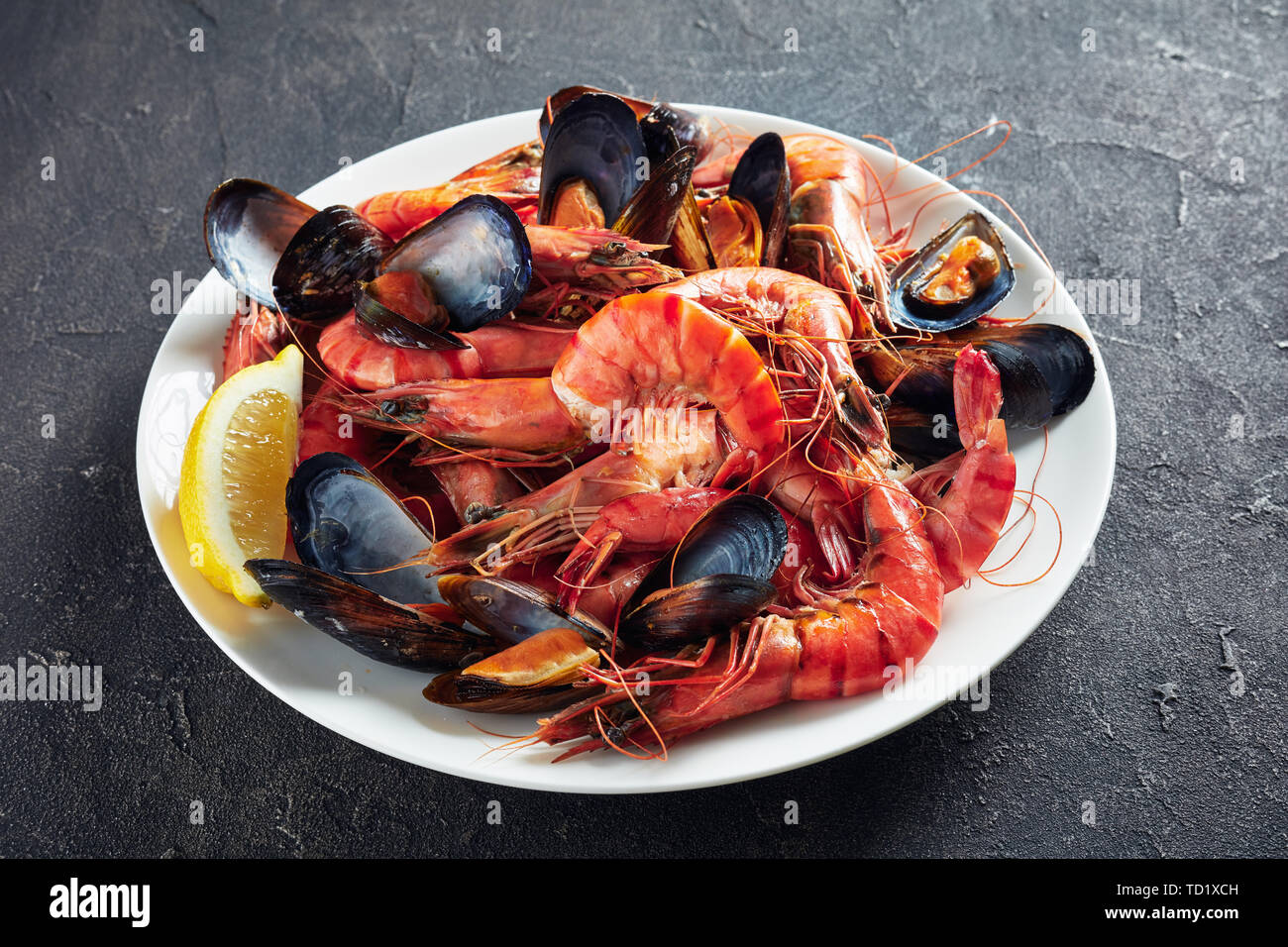 Nahaufnahme der Gemischte Meeresfrüchte - Muscheln, Muscheln und Garnelen auf einem weißen Teller auf einer konkreten Tabelle Stockfoto