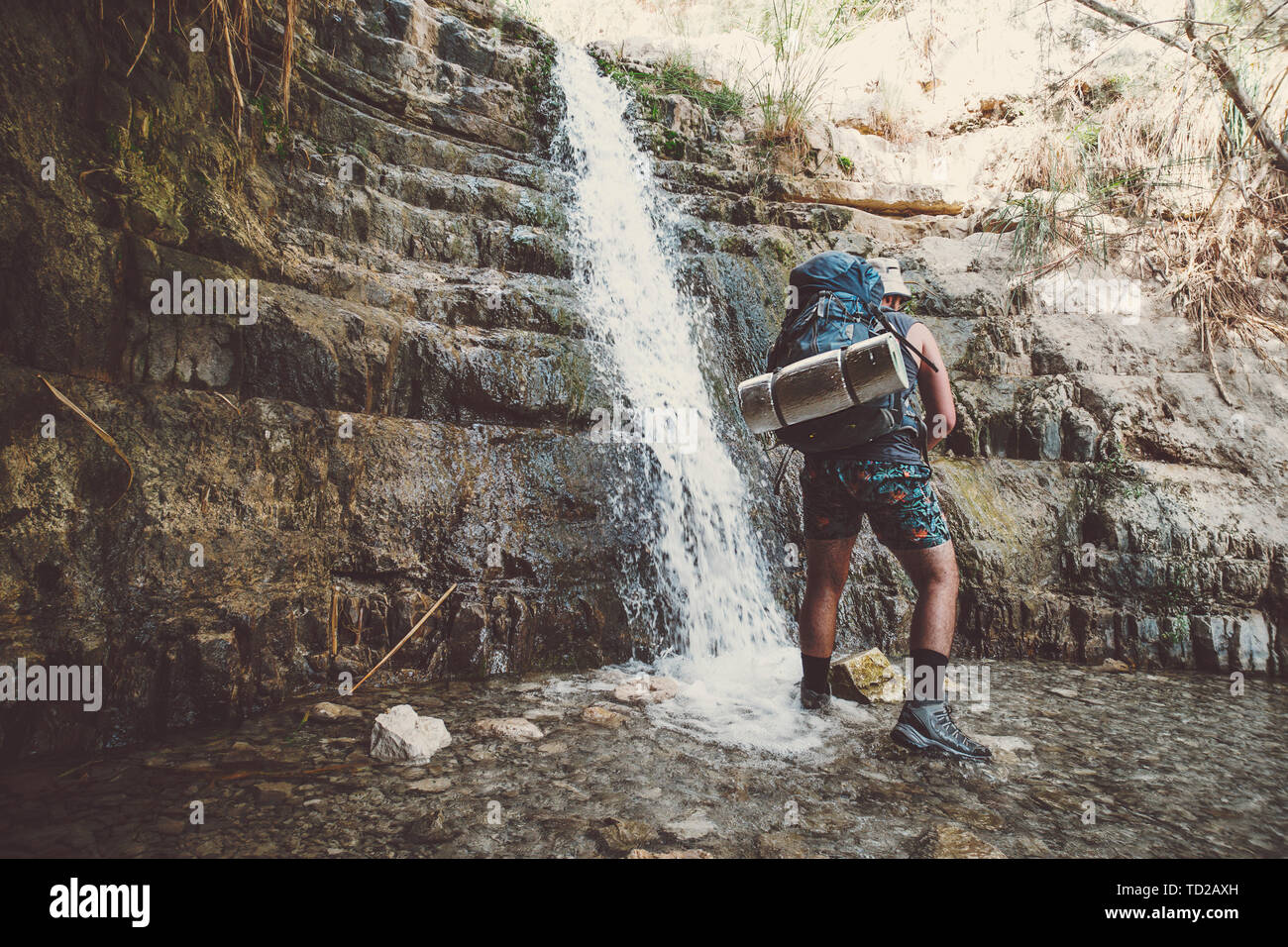 Alleinreisender Mann stand in der Nähe von Great Falls Shulamit fallen in einem flachen Teich mit smaragdgrünem Wasser. Ein Gedi - Naturpark und Nationalpark Stockfoto