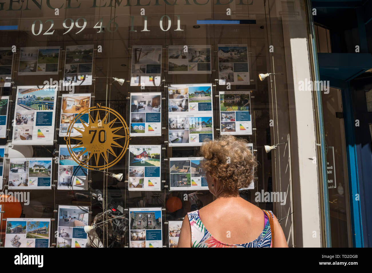 Eine Frau auf der Suche nach Details im Fenster der Immobilienmakler, Dinard, Bretagne, Frankreich Stockfoto