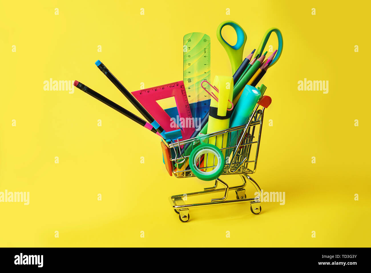 Zurück Konzept mit Warenkorb und Bunte Bleistifte zur Schule, Quadrat Lineal, Schere, Clips, Markierungen auf Pastellgelb Kulisse. Stockfoto