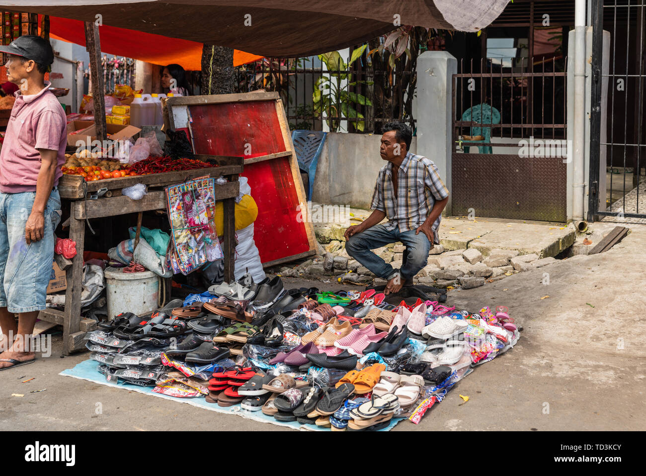Makassar, Sulawesi, Indonesien - 28. Februar 2019: Terong Street Market. Ambulante männlichen Schuh Anbieter hat einen Stapel der Schuhe auf eine Plane auf den Straßen verbreiten Stockfoto