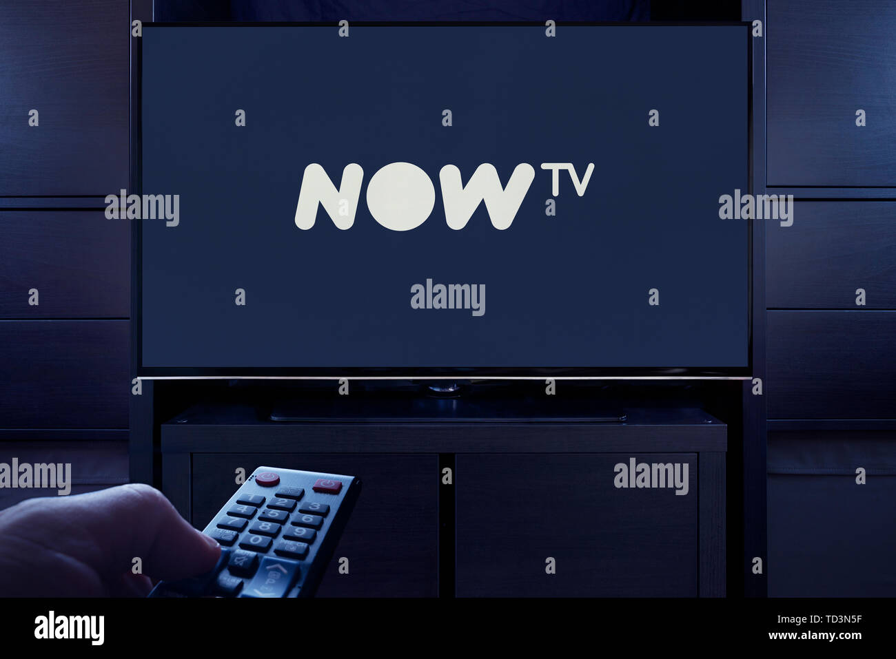 Ein Mann Punkte eine TV-Fernbedienung auf den Fernseher, die zeigt das Logo für die Jetzt TV on Demand Video Streaming Service (nur redaktionelle Nutzung). Stockfoto