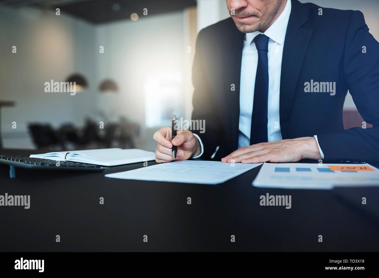 Nahaufnahme eines Geschäftsmannes Unterzeichnung Papiere und über Dokumente während der Arbeit an seinem Schreibtisch in einem hellen modernen Büro Stockfoto