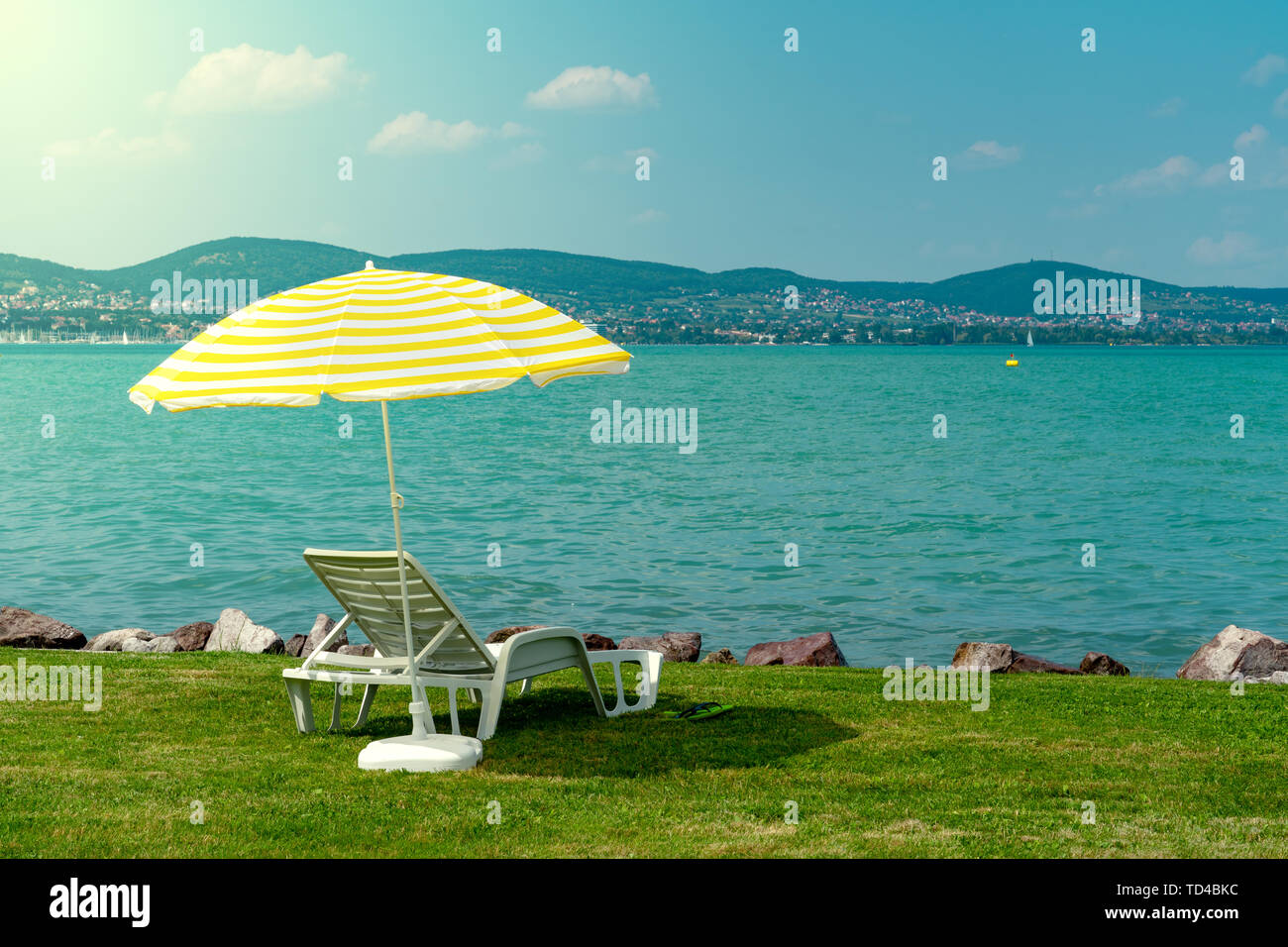 Stilvolle liege Kunststoff liege mit gelben Streifen Sonnenschirm Sonnenschirm auf dem grünen Rasen am Strand im Sommer unter freiem Himmel. Vorgesehen für die Sonnenliege Stockfoto