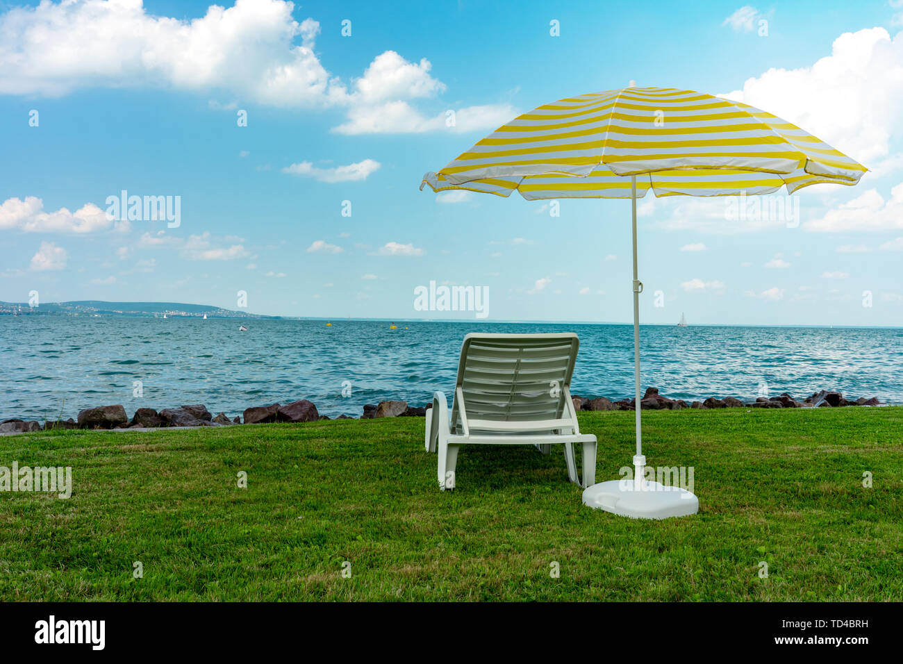 Stilvolle liege Kunststoff liege mit gelben Streifen Sonnenschirm Sonnenschirm auf dem grünen Rasen am Strand im Sommer unter freiem Himmel. Vorgesehen für die Sonnenliege Stockfoto