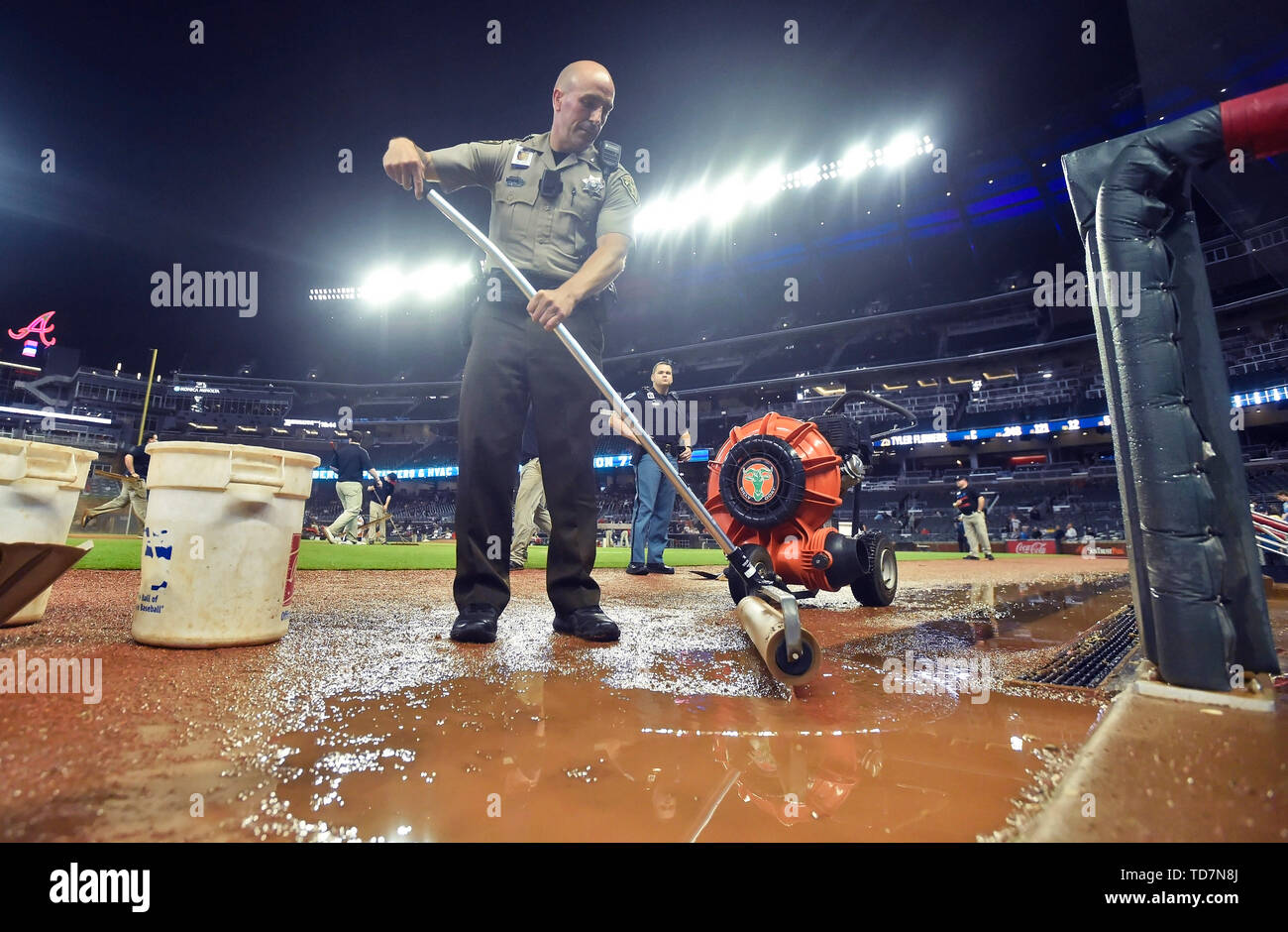 Atlanta, GA, USA. 12 Juni, 2019. Ein Cobb County Sheriff stellvertretender hilft, Wasser in einen Abfluss während einer siebten Inning Regen verzögert sich der MLB Spiel zwischen den Pittsburgh Pirates und Atlanta Braves bei SunTrust Park in Atlanta, GA. Austin McAfee/CSM/Alamy leben Nachrichten Stockfoto