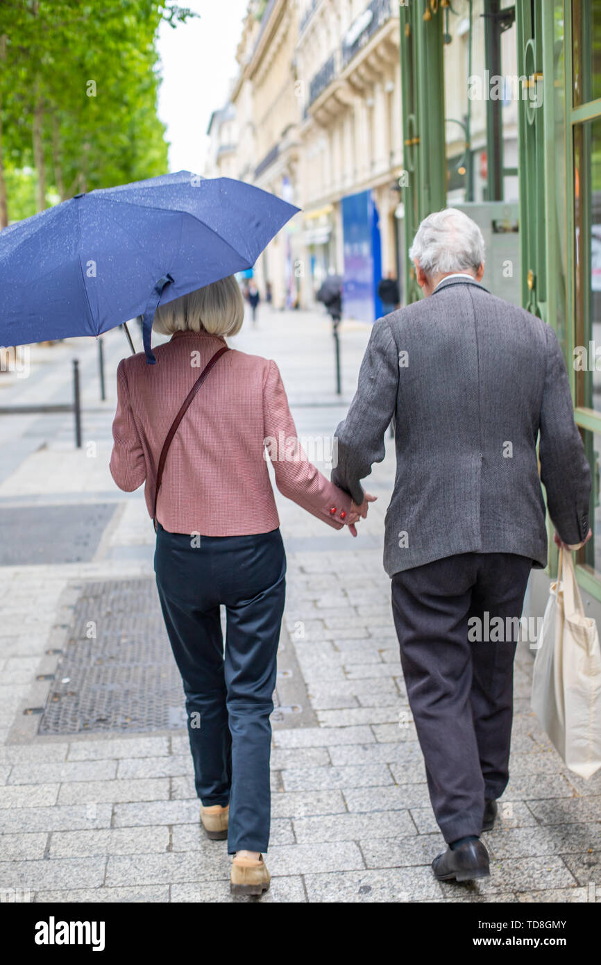 Ältere Paare unter dem Dach halten sich an den Händen. Lieben alten Menschen gehen die Straße hinunter. Stockfoto