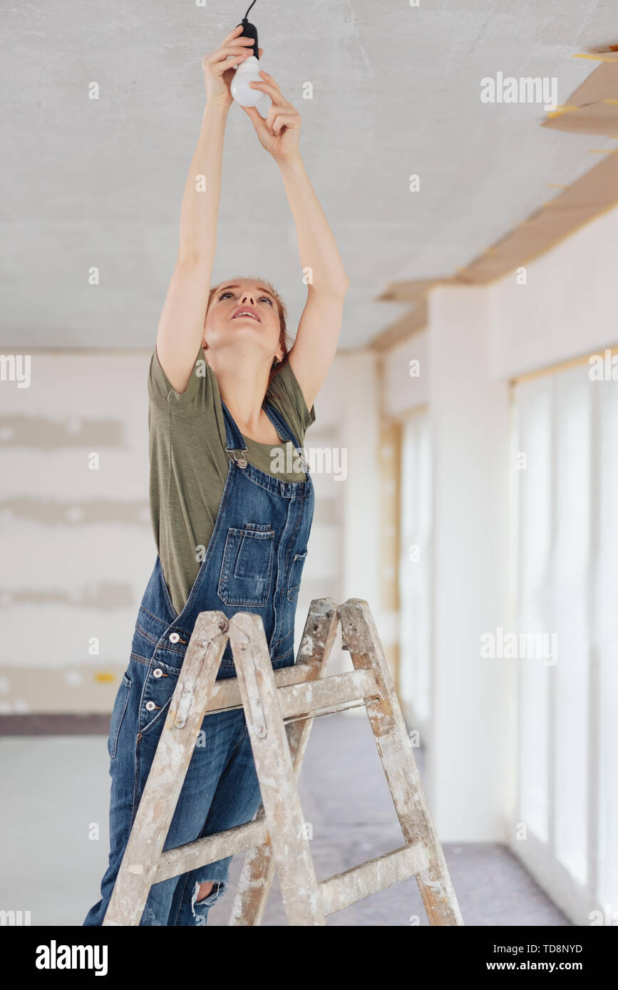 Junge Frau trägt Latzhose Austausch von Lampe beim Stehen auf der Leiter  bei einer einfachen Renovierung Stockfotografie - Alamy