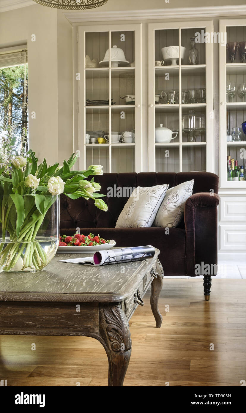 Weiße Tulpen in großen, durchsichtigen Glas Vase auf hölzernen Tisch vor getuftete Sofa im Wohnzimmer britische und irische NUR RECHTE Stockfoto