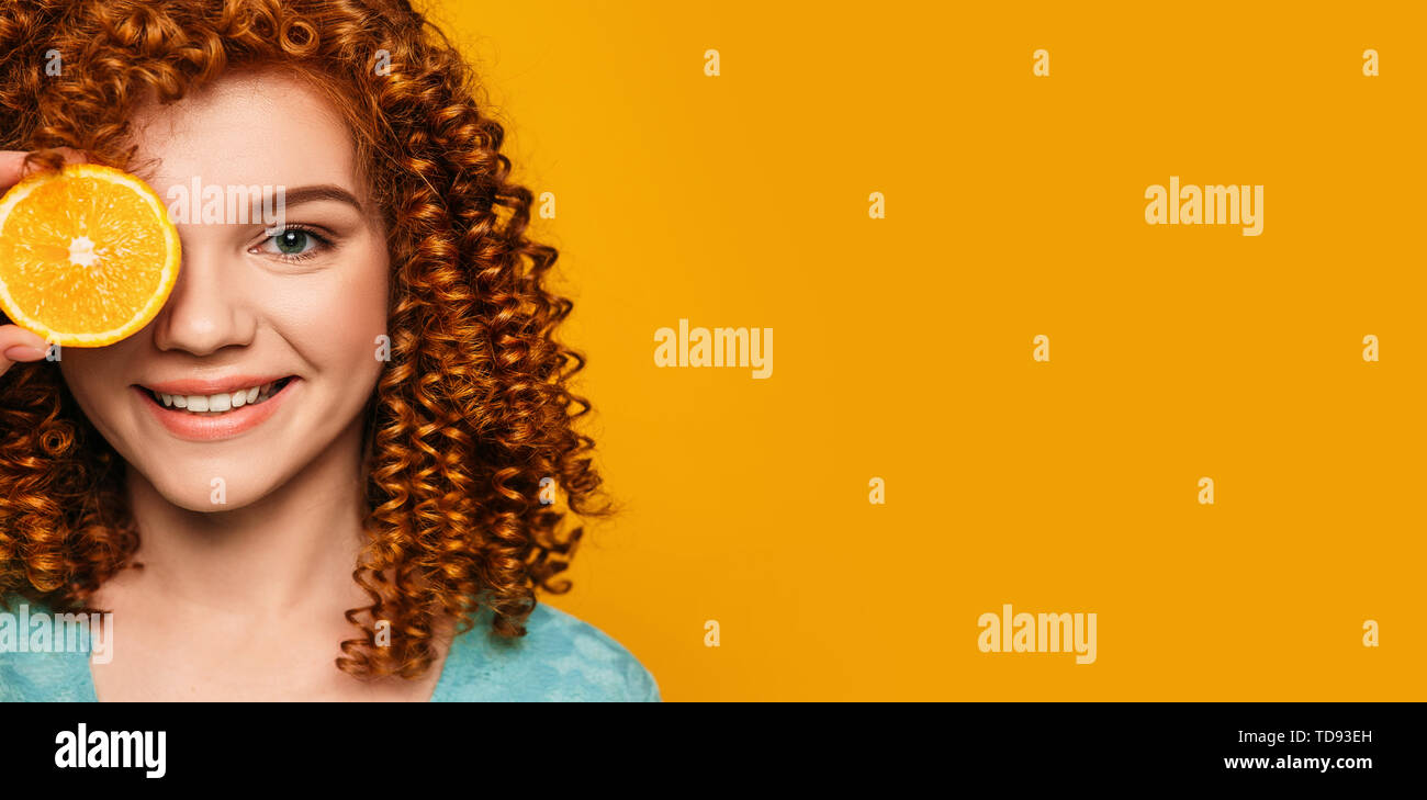 Curly rothaarige Frau mit einem orangen in der Nähe der Fläche auf einem gelben Hintergrund. Stockfoto