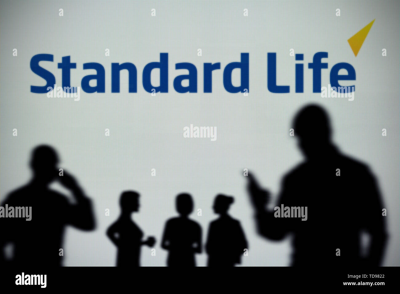 Die Standard Life Logo ist auf einen LED-Bildschirm im Hintergrund, während eine Silhouette Person ein Smartphone verwendet im Vordergrund (nur redaktionelle Nutzung) Stockfoto