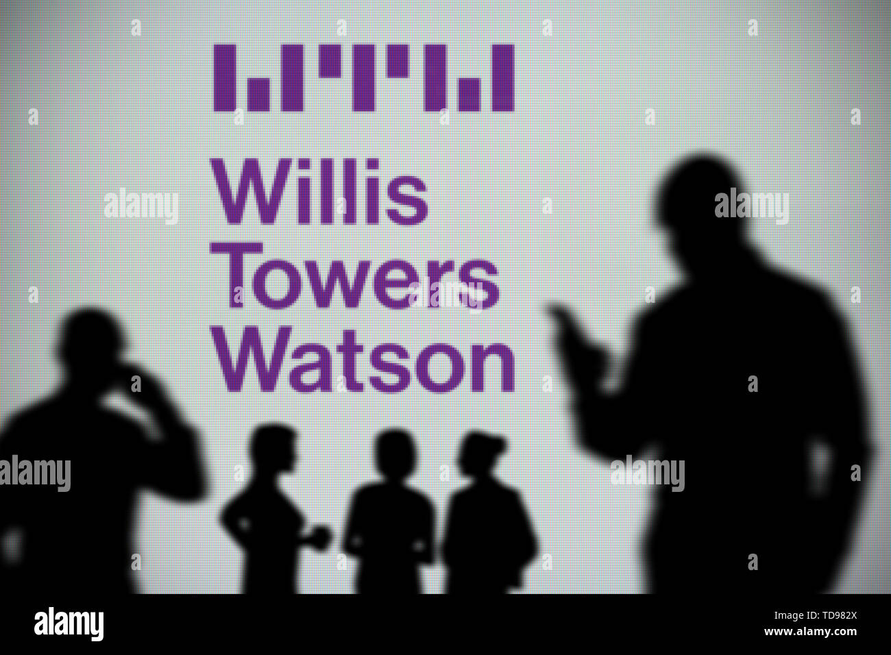 Die Willis Towers Watson Logo ist auf einen LED-Bildschirm im Hintergrund, während eine Silhouette Person ein Smartphone verwendet (nur redaktionelle Nutzung) Stockfoto
