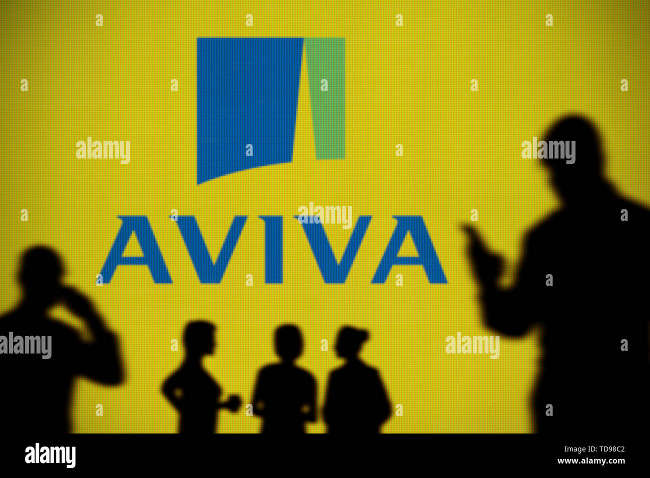 Das Aviva Insurance Logo ist auf einen LED-Bildschirm im Hintergrund, während eine Silhouette Person ein Smartphone im Vordergrund (nur redaktionelle Verwendung verwendet Stockfoto